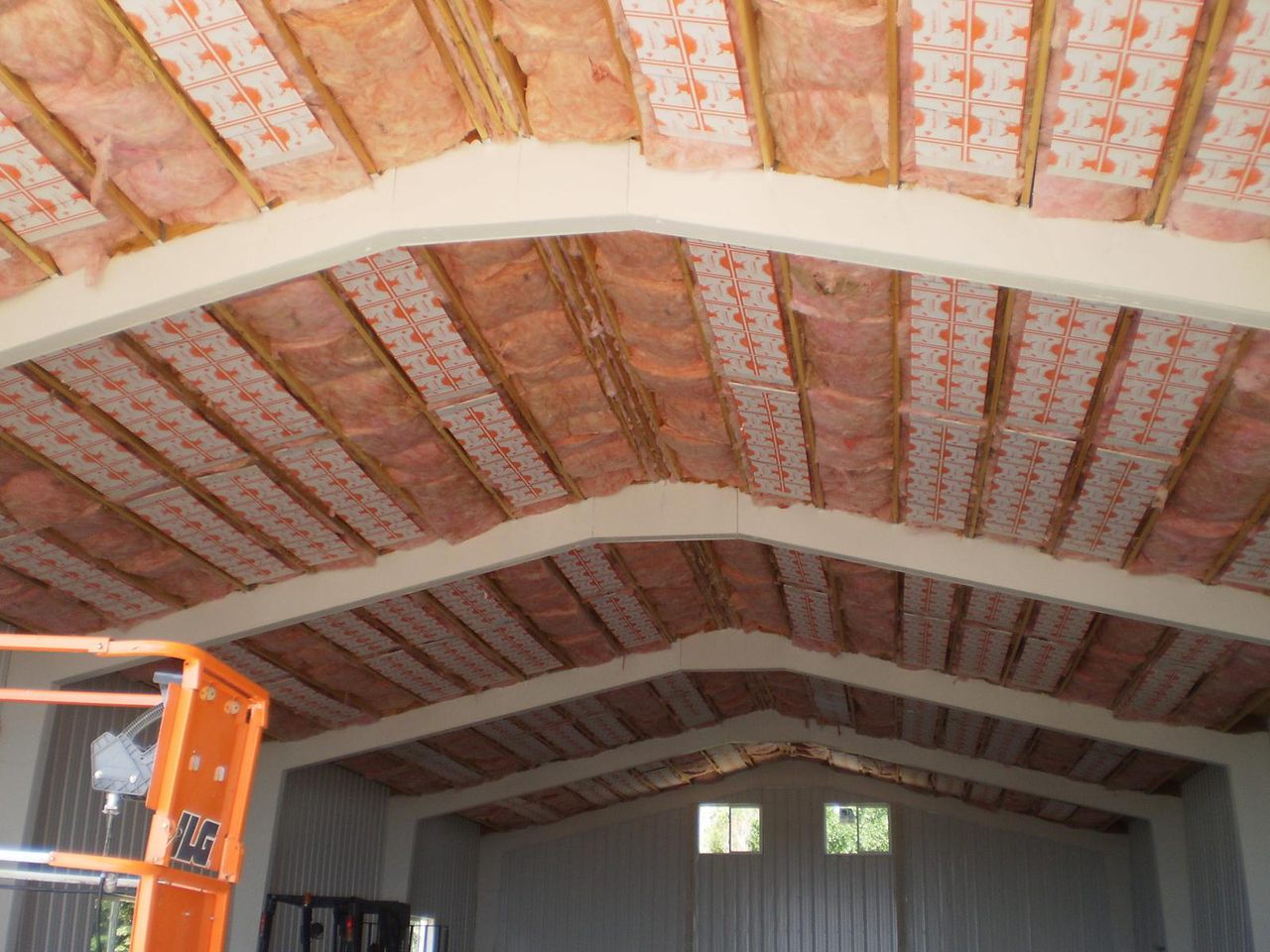 Radiant ceiling panels under pink insulation in the arched roof of a steel building