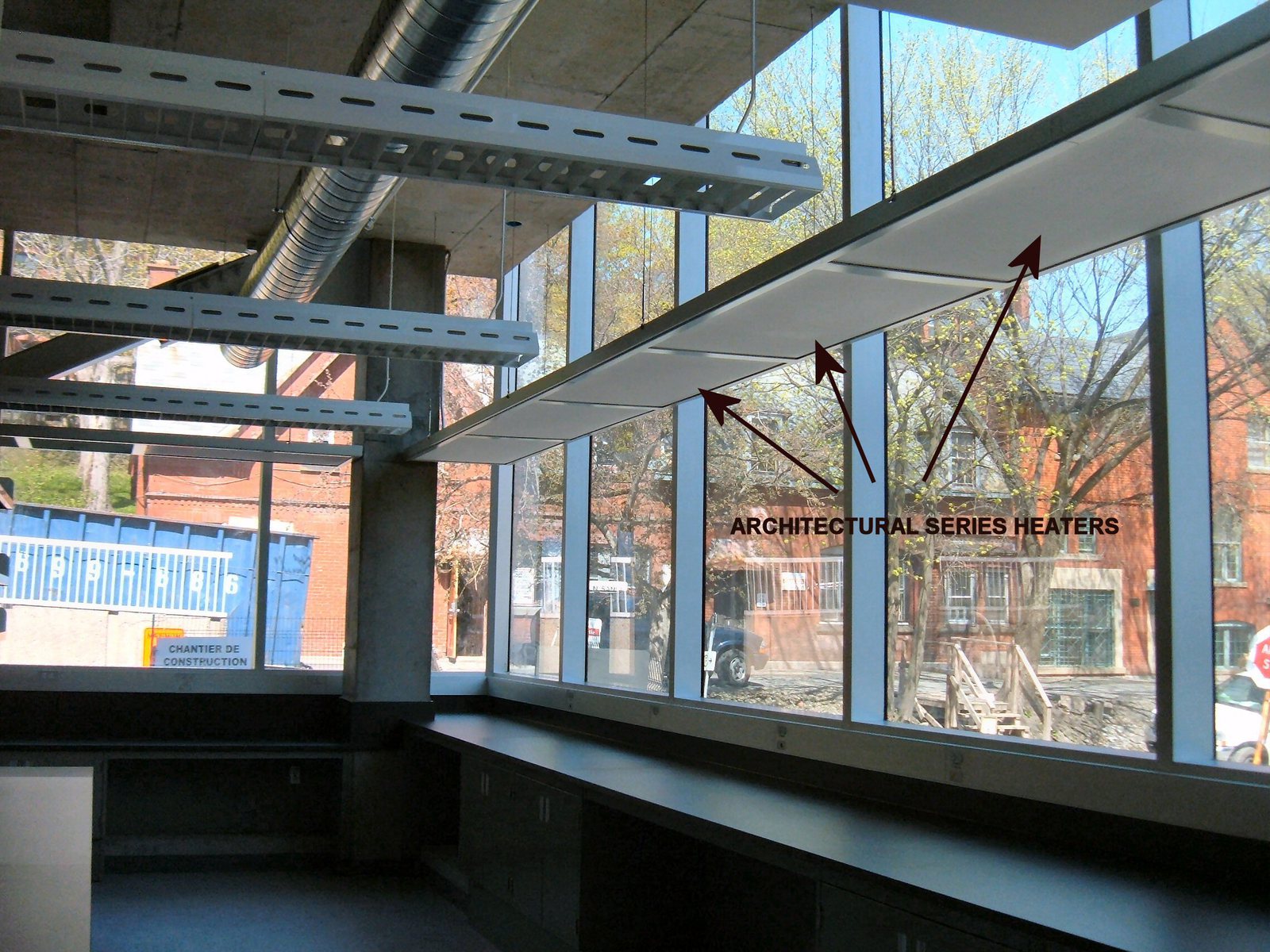 ThermaRay Architectural Series radiant heaters hung on cables along the window wall of a lab, with arrows pointing to the heaters