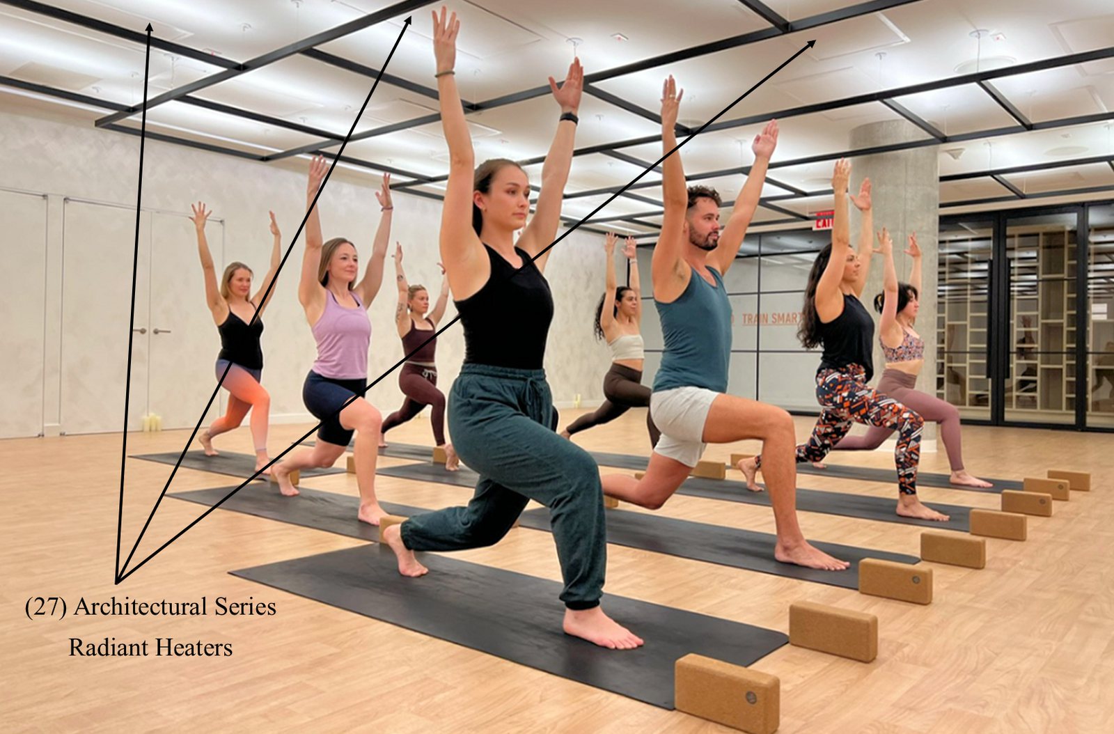 Yoga class in a studio with 27 Architectural Series radiant heaters recessed into the ceiling, marked with arrows