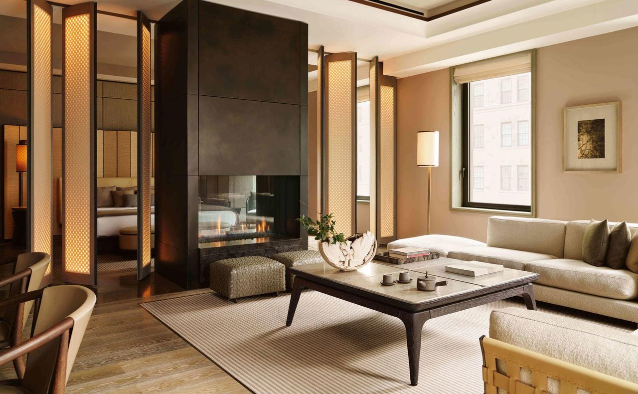 Living room of a corner suite at Aman New York, with a fireplace and tall windows
