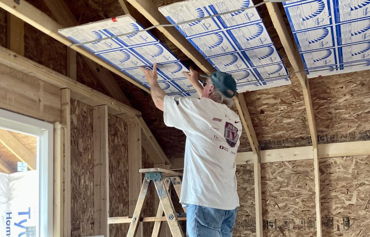 Dan placing a ThermaRay panel between ceiling joists in a framed room