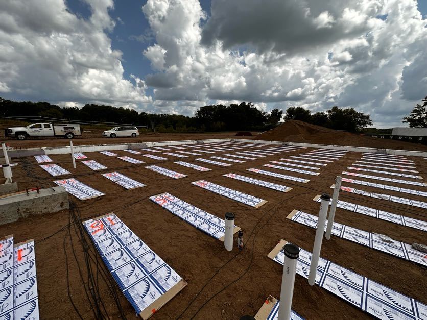 Heating panels laid out on the sand with plumbing stubs, under a cloudy sky