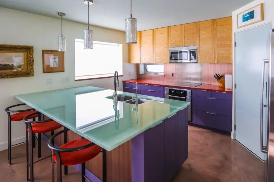 Kitchen with a glass-topped island, red stools and purple cabinets